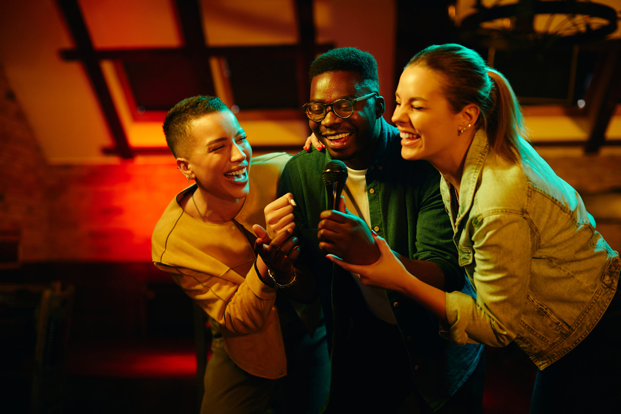 Young happy people having fun and singing karaoke while being in a pub at night. Personnes chantant des chansons incontournables en karaoké